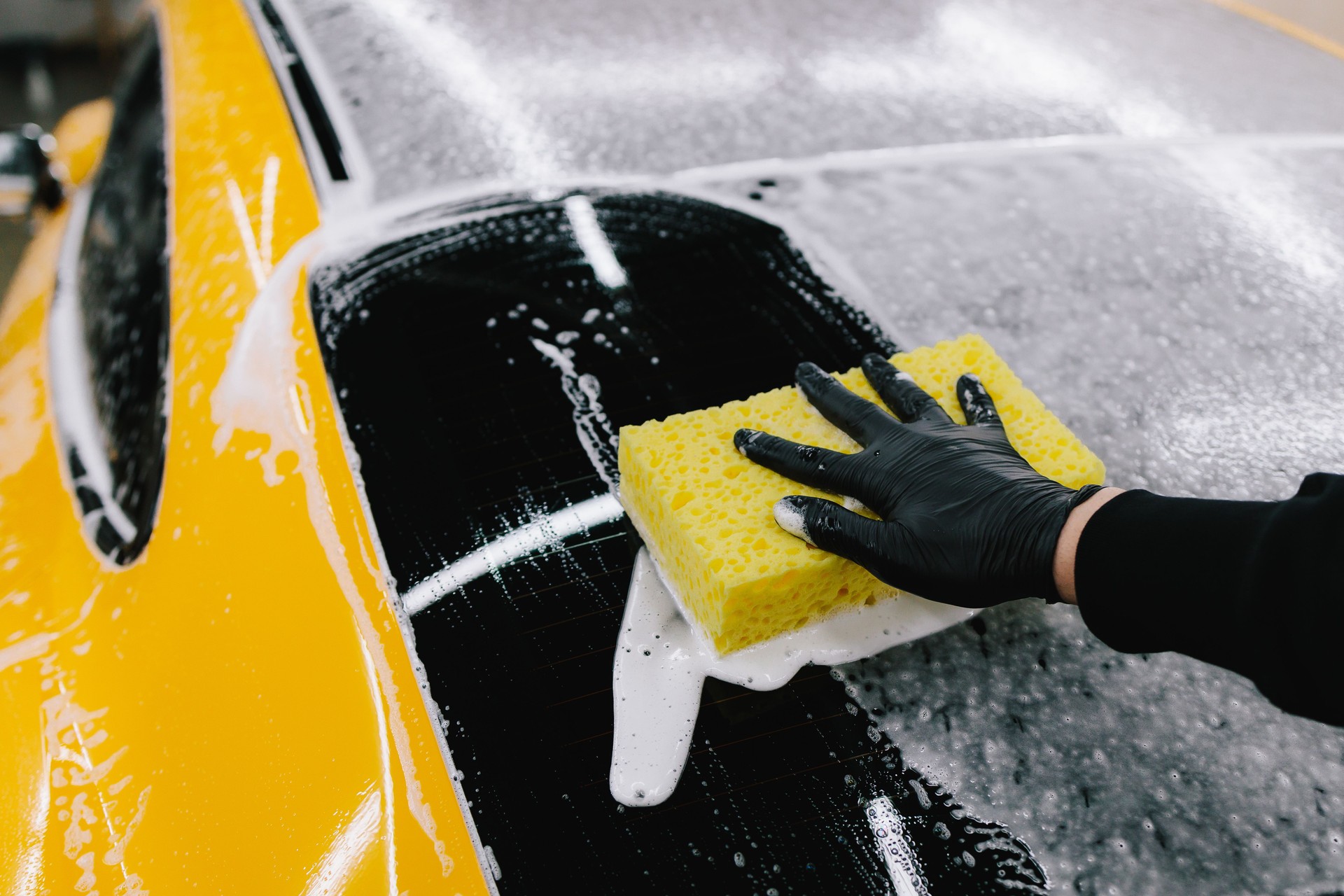 Sports car manual hand washing using foam and detergent with yellow sponge at the car washing service. Detailing sports car with foam at the auto service.