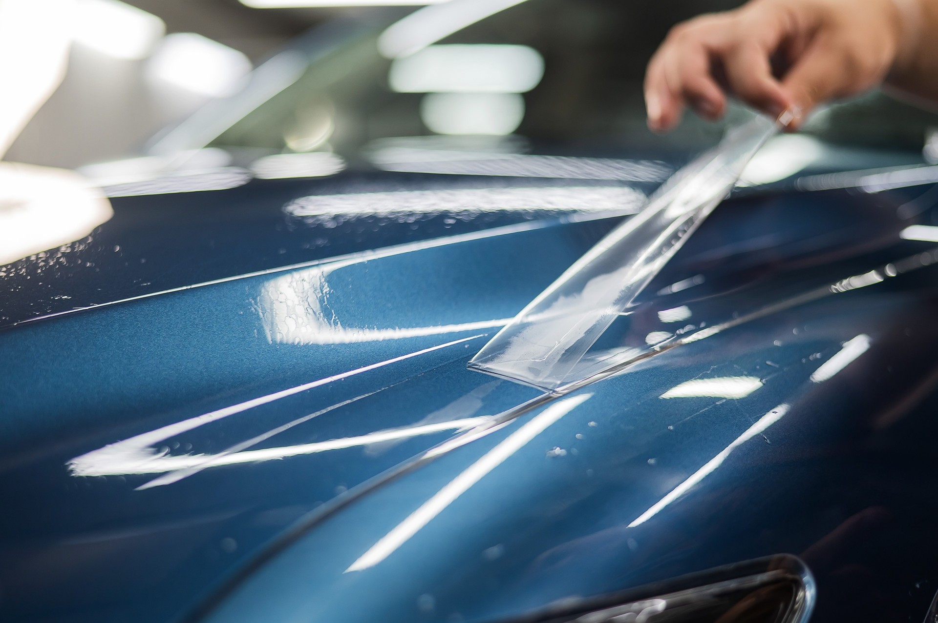 The master in the car service applies a protective armor film to the car body.