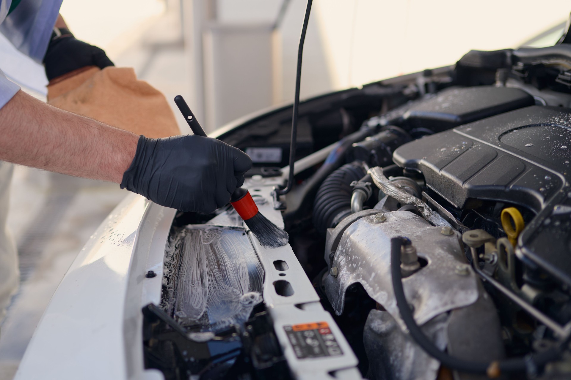 Car detailer cleaning engine compartment with brush and detergent
